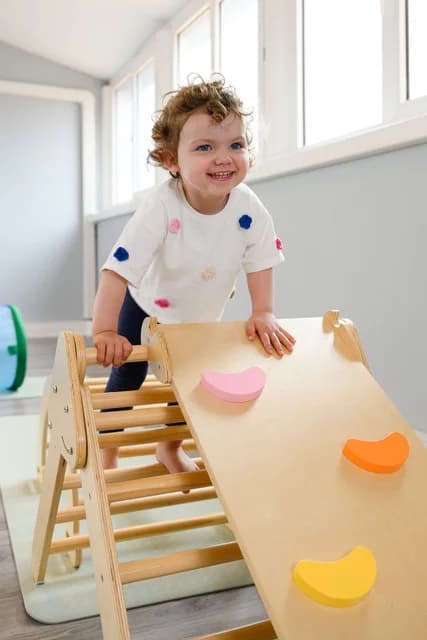 Tout-petit souriant qui grimpe sur un module de motricité en bois au studio