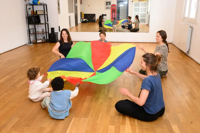 Séance de baby gym en groupe : parents et tout-petits jouent avec un parachute coloré au studio