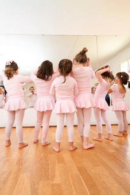 Groupe de jeunes danseuses en tenue rose, de dos face au miroir du studio