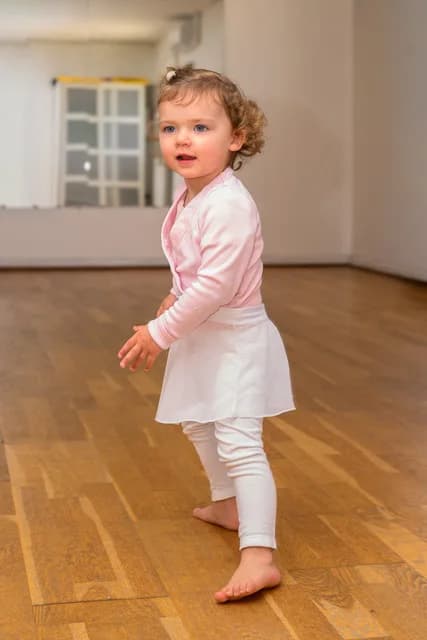 Tout-petit en tenue de danse rose et blanc, debout sur le parquet du studio