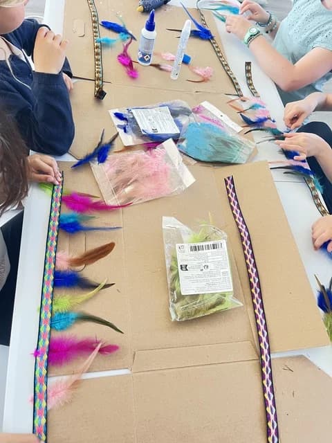 Enfants fabriquant des accessoires colorés en plumes autour d'une table pendant le stage